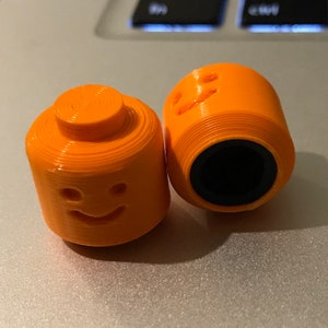 May include: Two orange plastic toy figures shaped like Lego minifigures. One figure has a smiling face and the other has a blank face.
