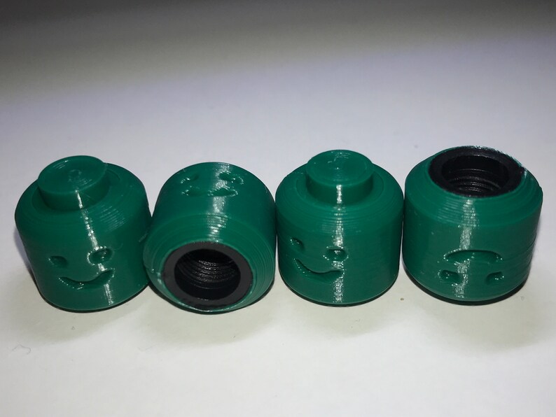 May include: Four green plastic bottle caps with different facial expressions. Each cap has a threaded opening on the bottom.