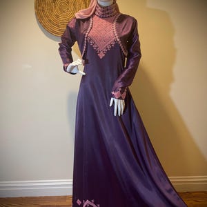 May include: A long, purple satin dress with pink embroidery. The dress has a high neckline and long sleeves. The embroidery is in a geometric pattern and is around the neckline, sleeves, and hem of the dress.