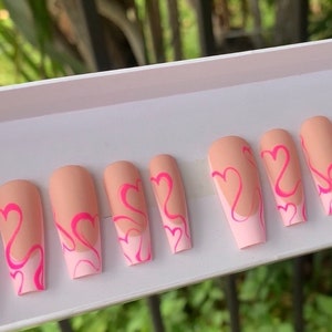 May include: A set of ten nude-colored false nails with a white tip and pink heart designs.