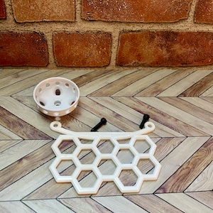 Puede incluir: Estante de pl&aacute;stico blanco en forma de panal con dos tornillos negros. La estanter&iacute;a tiene una parte superior curva y una parte inferior redondeada. Hay una maceta redonda de pl&aacute;stico blanco con agujeros en el lateral.