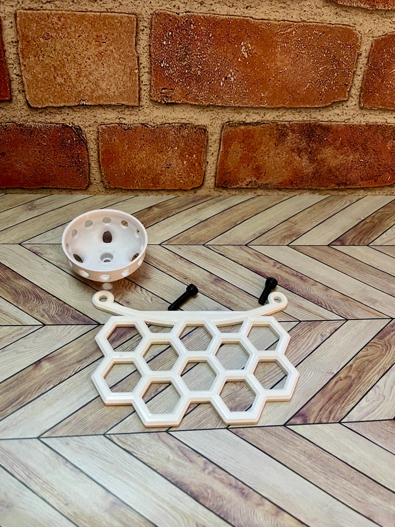 Puede incluir: Estante de pl&aacute;stico blanco en forma de panal con dos tornillos negros. La estanter&iacute;a tiene una parte superior curva y una parte inferior redondeada. Hay una maceta redonda de pl&aacute;stico blanco con agujeros en el lateral.