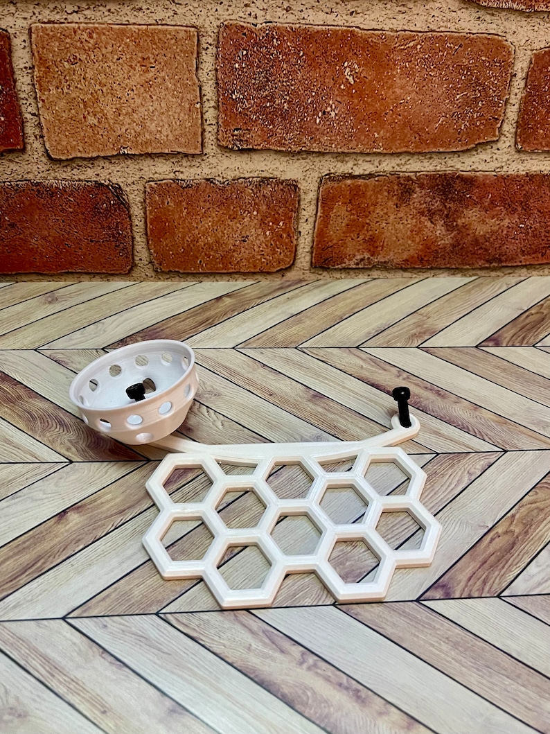 Puede incluir: Plato blanco de pl&aacute;stico en forma de panal con un peque&ntilde;o cuenco blanco de pl&aacute;stico con agujeros. El plato y el cuenco est&aacute;n sobre un suelo de madera.
