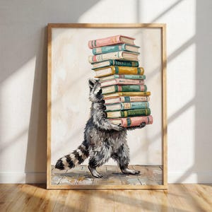 Könnte beinhalten: Ein gerahmtes Gemälde eines grau-schwarzen Waschbären, der auf seinen Hinterbeinen steht und einen hohen, wackeligen Stapel aus zwölf bunten Hardcover-Büchern balanciert. Die Bücher haben verschiedene Pastell- und gedeckte Töne, darunter Rosa, Blau, Grün und Gelb.