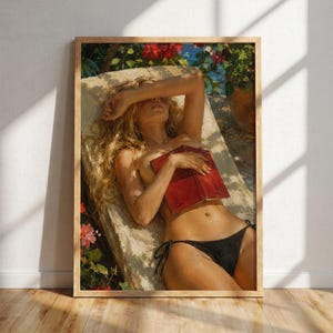 May include: A framed art print depicts a person reclining on a lounge chair, holding a red book. The person wears a black bikini bottom. The background features flowers and a glimpse of the sea. The artwork is in a wooden frame.
