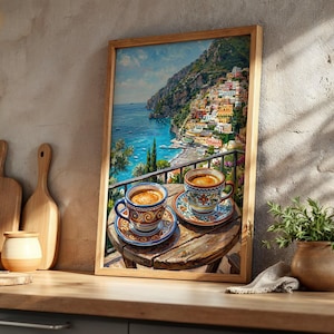 Puede incluir: Una l&aacute;mina de arte enmarcada que representa un pueblo costero italiano con edificios coloridos en un acantilado sobre el mar. En primer plano, dos tazas de caf&eacute; de cer&aacute;mica con motivos y platillos sobre una peque&ntilde;a mesa de madera.
