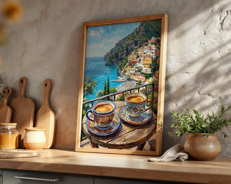 Puede incluir: Una l&aacute;mina de arte enmarcada que representa un pueblo costero italiano con edificios coloridos en un acantilado sobre el mar. En primer plano, dos tazas de caf&eacute; de cer&aacute;mica con motivos y platillos sobre una peque&ntilde;a mesa de madera.