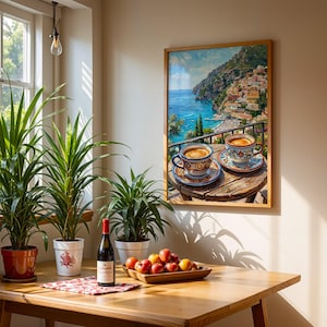 Puede incluir: Un cuadro de pared enmarcado que representa dos tazas de caf&eacute; sobre una mesa de madera con vistas a una ciudad costera, expuesto sobre una mesa de madera con tres plantas en macetas, una botella de vino tinto y un cuenco de madera con frutas.