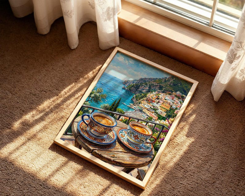 Puede incluir: Una impresi&oacute;n rectangular enmarcada que presenta una vibrante escena costera con dos tazas de caf&eacute; de cer&aacute;mica sobre una mesa de madera. La obra muestra un pueblo mediterr&aacute;neo en la ladera con vistas al mar azul y motivos florales detallados.