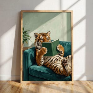 May include: A framed wall art print featuring an orange and black tiger sitting on a teal armchair while holding an open green book. The tiger has its paws on the book pages, and a green potted plant is visible in the background corner.