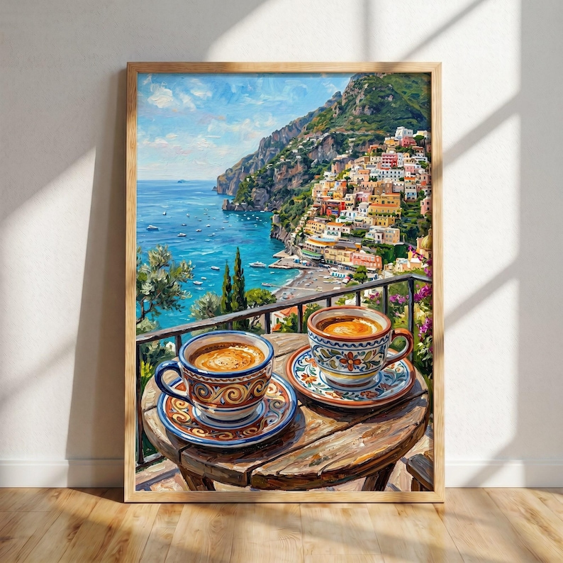 Puede incluir: Un cuadro enmarcado que representa dos tazas de caf&eacute; de cer&aacute;mica con intrincados motivos florales sobre una mesa de madera. El fondo muestra una ciudad costera construida en una ladera escarpada sobre un mar azul bajo un cielo nublado.