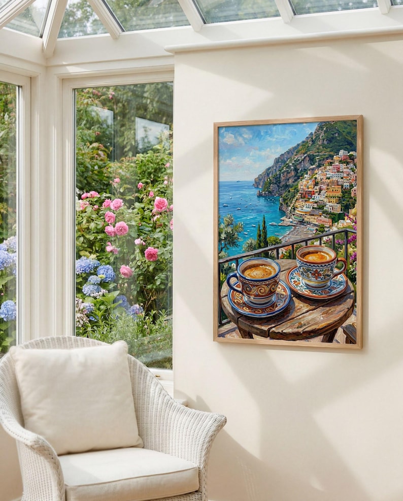 Puede incluir: Una impresi&oacute;n art&iacute;stica enmarcada que representa una escena costera mediterr&aacute;nea con dos tazas de caf&eacute; de cer&aacute;mica estampadas sobre una peque&ntilde;a mesa de madera, con vistas a una ciudad en la ladera con edificios coloridos y un mar azul.