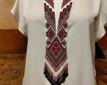 May include: A long, beaded necklace with a geometric pattern in red, white, and black. The necklace is made of small, round beads and has a fringe at the bottom.