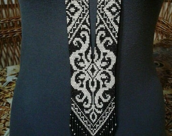 May include: A long black and white beaded necklace with a geometric pattern and a fringe at the bottom.