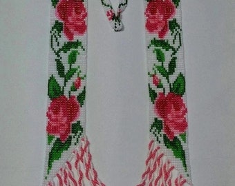 May include: A white beaded necklace with pink and green floral designs. The necklace has a long, cascading fringe of white and pink beads.