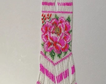 May include: A white beaded necklace with pink and green floral designs. The necklace has a long fringe at the bottom.