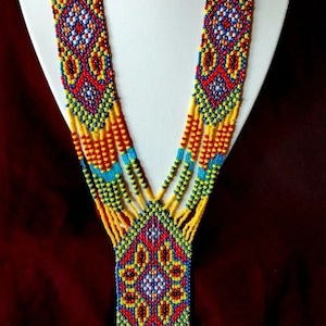 May include: A multi-strand beaded necklace featuring a geometric pattern in shades of yellow, red, blue, and white. The necklace has a long, teardrop-shaped pendant with a similar design.