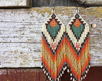 May include: A pair of long, beaded earrings with a geometric pattern in shades of orange, brown, white, and turquoise.