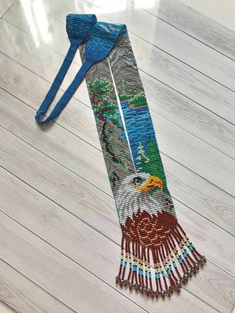 May include: A beaded lanyard featuring a blue, white and green beaded image of a bald eagle with a red, white and blue fringe.