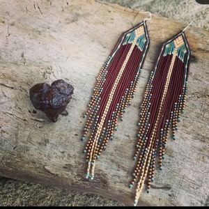 May include: A pair of long, beaded earrings with a geometric design. The earrings are made with brown, gold, and turquoise beads.