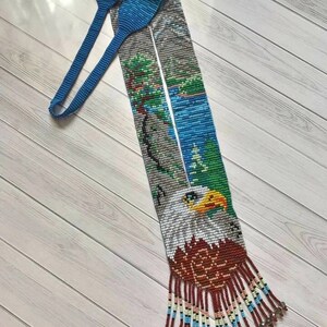 May include: A beaded lanyard featuring a blue, white and green beaded image of a bald eagle with a red, white and blue fringe.