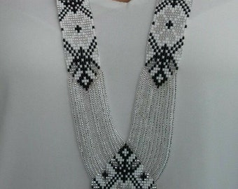 May include: A long, beaded necklace with a geometric pattern in black and white. The necklace has a fringe at the bottom and is made of silver beads.