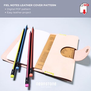 Puede incluir: Una funda de cuaderno de cuero rosa claro con una solapa, abierta para revelar páginas rayadas. Varios lápices amarillos, azules, rojos y rosas se colocan junto al cuaderno. El texto "FIEL NOTES LEATHER COVER PATTERN" está en la parte superior.
