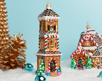 May include: A set of two gingerbread house Christmas ornaments. The larger ornament is a tall, multi-tiered gingerbread house with candy cane accents. The smaller ornament is a single-story gingerbread house with a heart-shaped door. Both ornaments are decorated with colorful icing and candy.