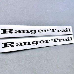 May include: Two rectangular, silver-colored decals with the words "Ranger Trail" printed in bold, black letters. The decals are positioned side-by-side against a light gray background.