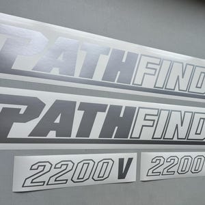 May include: Silver and white PATHFINDER and 2200V decals. The PATHFINDER decals are long and rectangular, with the word in a bold, outlined font. The 2200V decals are smaller and feature the number in a similar font.