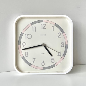 Puede incluir: Reloj cuadrado Kienzle de cuarzo blanco con esfera color crema. La esfera presenta números negros, manecillas negras y un anillo de acento rosa y gris. El reloj es de diseño clásico.