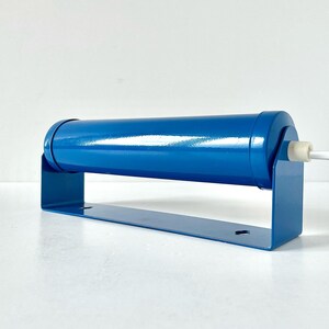 May include: A blue metal wall lamp with a cylindrical shade and a simple bracket. The lamp has a white wire cord.