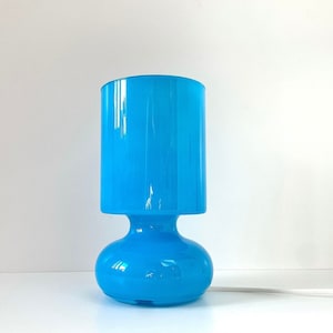 May include: A bright blue glass table lamp with a rounded base and a cylindrical shade.