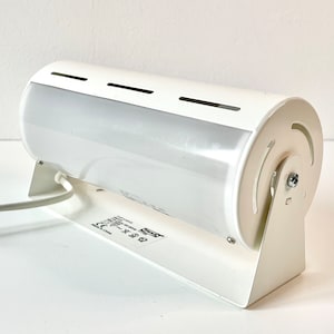 May include: White wall-mounted lamp with a cylindrical shade and a swiveling base. The lamp has a white cord and a label with the text "8.8W" and "CE".