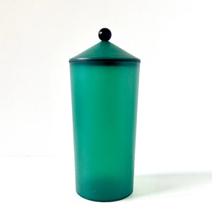 Puede incluir: Un recipiente de plástico verde con una perilla negra en la tapa. El recipiente es cilíndrico y tiene una superficie lisa.