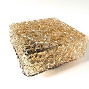 May include: A square, amber-colored glass light fixture with a textured, bubbly surface. The fixture is made of multiple small, irregular glass pieces, creating a unique, decorative design. The light fixture is likely for indoor use.