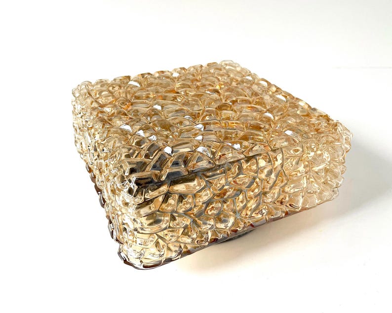 May include: A square, amber-colored glass light fixture with a textured, bubbly surface. The fixture is made of multiple small, irregular glass pieces, creating a unique, decorative design. The light fixture is likely for indoor use.