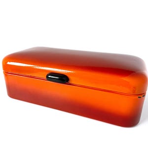 May include: A rectangular, glossy orange box with a black clasp. The box has a gradient effect, transitioning from a deep red at the base to a bright orange at the top. The lid is slightly rounded.