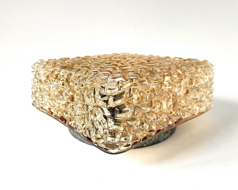 May include: A vintage, square-shaped light fixture with a textured, amber-colored glass shade. The shade has a bubbly, irregular surface. The fixture is mounted on a circular, gray metal base, creating a mid-century modern aesthetic.