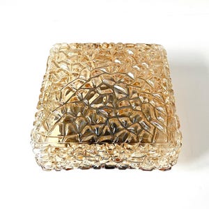 May include: A square-shaped, amber-colored glass lampshade with a textured, geometric pattern. The shade has a slightly flared shape and a warm, inviting glow. The design is reminiscent of cut crystal or faceted glass.