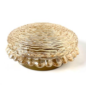 May include: A vintage, amber-colored glass light fixture. The fixture has a textured, ridged dome-shaped shade and a scalloped edge. The base is a muted gold color. The light fixture is designed to be mounted on a ceiling.
