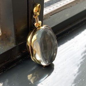 May include: A gold locket with a clear glass insert. The locket has a decorative, scalloped edge.