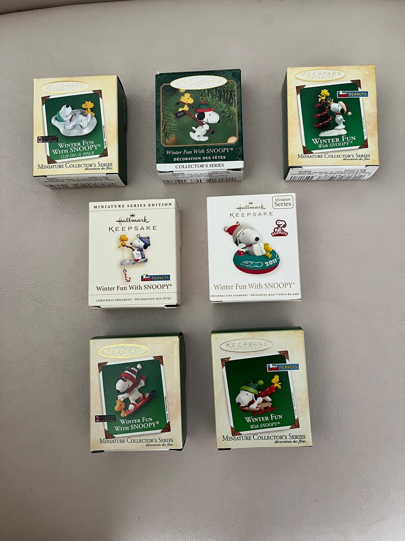 May include: Seven Hallmark Keepsake miniature collector's series boxes featuring Snoopy in winter scenes. The boxes are various colors, with Snoopy in different winter activities. The text "Winter Fun With Snoopy" is visible on the boxes.