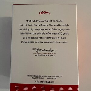 K&ouml;nnte beinhalten: Eine wei&szlig;e Box mit rotem Rand und einem rot-wei&szlig; gestreiften Rand. Die Box zeigt ein Zitat von Anita Marra Rogers, einer Keepsake-K&uuml;nstlerin, &uuml;ber ihre Liebe zum Modellieren. Die Box enth&auml;lt auch das Logo der Hallmark Marketing Company und die Worte "artist crafted & brass".