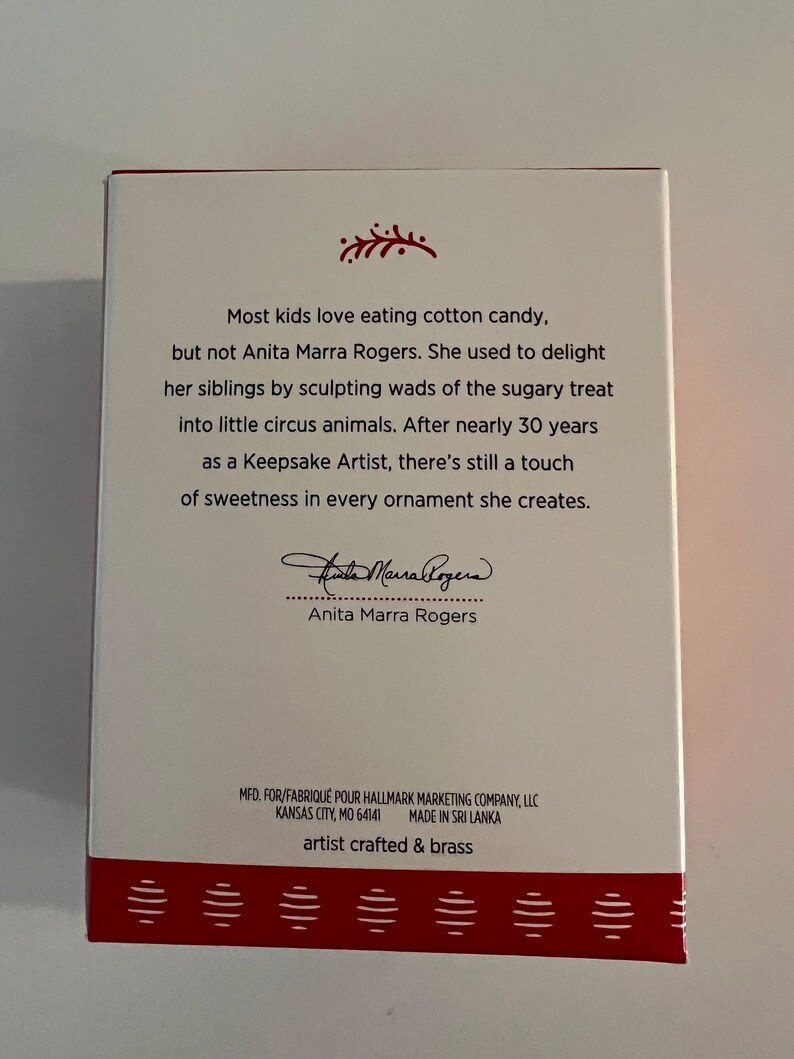 K&ouml;nnte beinhalten: Eine wei&szlig;e Box mit rotem Rand und einem rot-wei&szlig; gestreiften Rand. Die Box zeigt ein Zitat von Anita Marra Rogers, einer Keepsake-K&uuml;nstlerin, &uuml;ber ihre Liebe zum Modellieren. Die Box enth&auml;lt auch das Logo der Hallmark Marketing Company und die Worte "artist crafted & brass".
