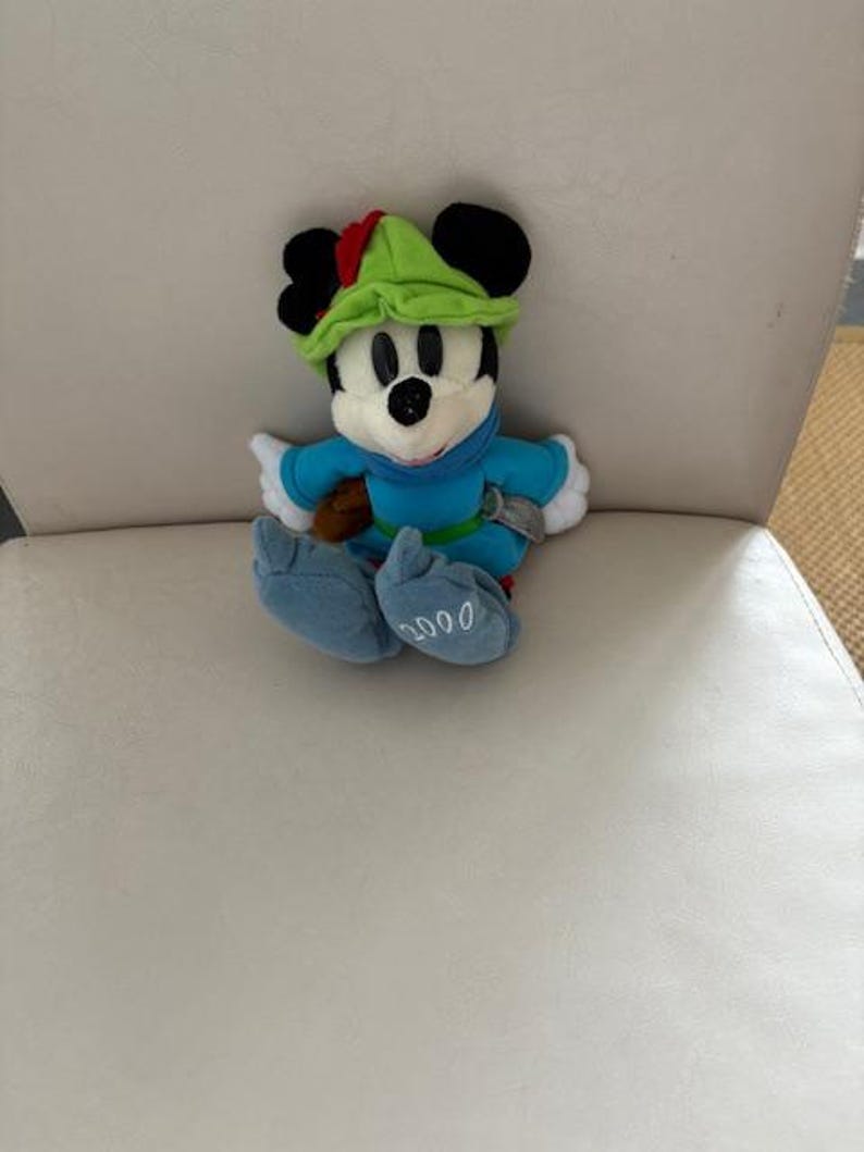 May include: A white ceramic mug with a black handle and the text "But First, Coffee" in a bold, black font. The mug is set against a blurred background, suggesting a cozy setting.