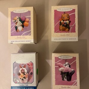 May include: Four small boxes with pink and white backgrounds featuring a Garden Club logo and the text "Collector's Series". Each box features a different animal figurine holding flowers: a squirrel, a skunk, a bunny, and a raccoon.