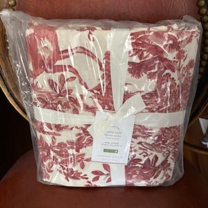 May include: A packaged duvet cover with a red and white toile pattern. The design features a pastoral scene with trees and figures. The packaging includes a white ribbon and a product tag that reads "pine toile duvet cover".