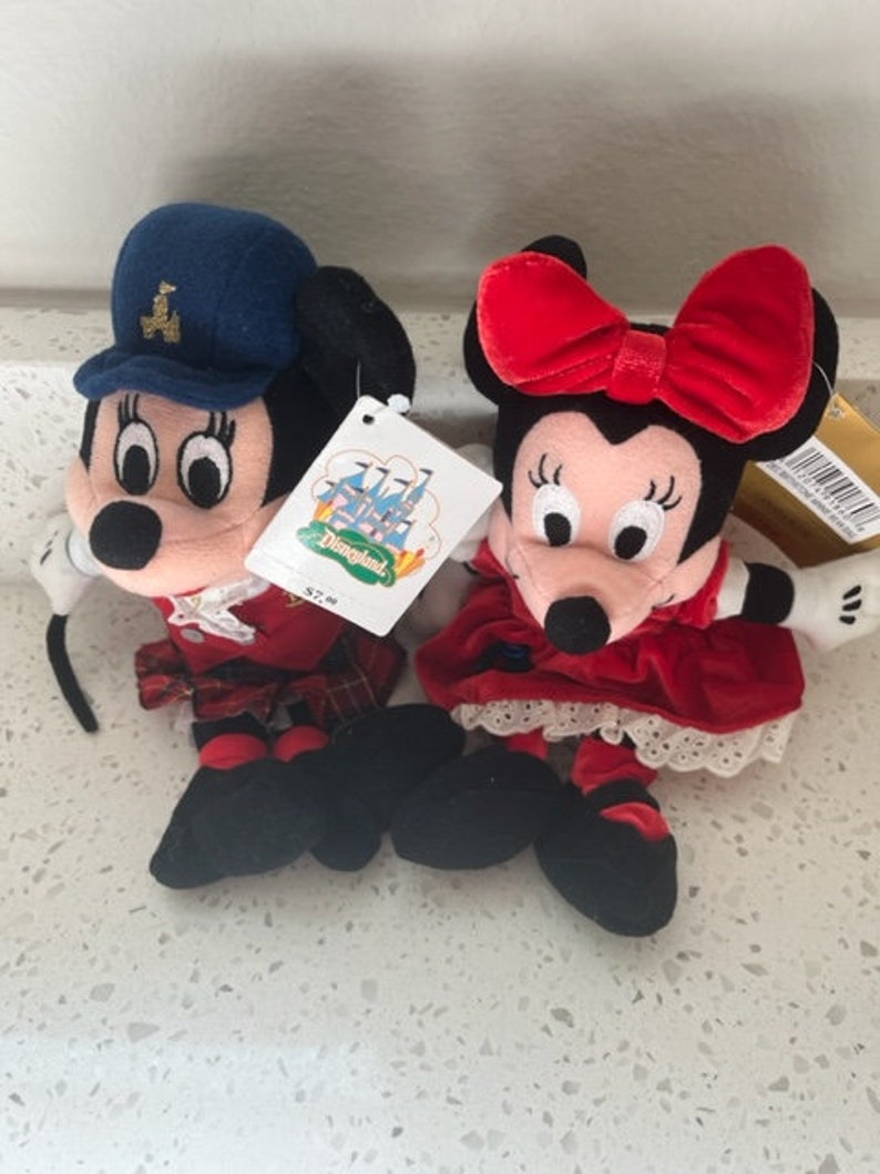 Puede incluir: Un par de peluches de Mickey Mouse y Minnie Mouse vestidos con faldas escocesas tradicionales y vestidos. Los juguetes llevan lazos rojos y sombreros. El juguete de Mickey Mouse lleva una peque&ntilde;a gaita. El juguete de Minnie Mouse lleva una peque&ntilde;a flor.