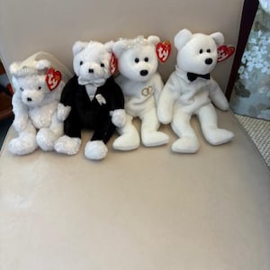 May include: Four white plush teddy bears, each with a Ty heart tag. One bear wears a bridal veil, another a tuxedo, and a third has wedding rings. The fourth bear has a black bow tie.